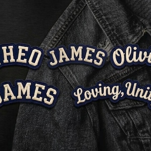 May include: Four navy blue and white embroidered patches with arched lettering. The patches display the text THEO JAMES, Olivia, JAMES, and Loving, Unity in a bold, collegiate-style font. These fabric patches feature a dark blue border.