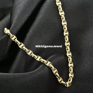 May include: A gold chain necklace with a nautical design, featuring interlocking links. The necklace is displayed on a black, textured fabric. The text "NikhilgemsJewel" is visible in the image.