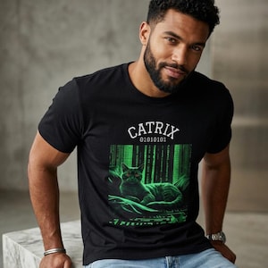 May include: Black t-shirt with a green and black graphic of a cat in a Matrix-style design. The word "CATRIX" is above the graphic, with "01010101" below it. The shirt is made of a soft material.