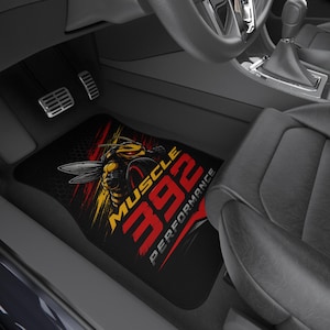 May include: A black car floor mat featuring a graphic of a yellow and black hornet with red accents. The text MUSCLE 392 PERFORMANCE is printed in bold red and yellow lettering across the mat, which is positioned in the footwell of a vehicle.
