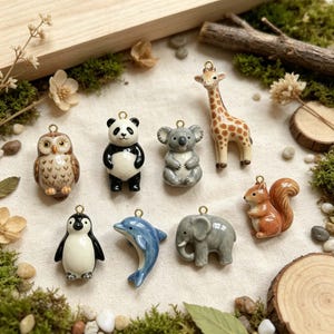 Puede incluir: Un conjunto de ocho dijes de cerámica con forma de búho, panda, koala, jirafa, pingüino, delfín, elefante y ardilla. Cada pequeña figura cuenta con una anilla de metal dorado en la parte superior para colgar los dijes con facilidad.