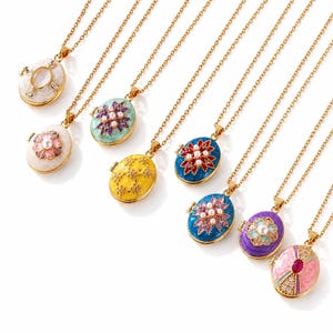 May include: A collection of eight oval-shaped locket necklaces on gold-tone chains. Each locket features unique enamel colors including white, mint green, yellow, blue, and purple, decorated with small pearls, crystals, and floral patterns.