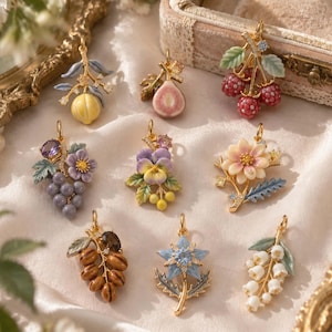 Peut inclure: Un ensemble de neuf pendentifs en métal doré avec des motifs botaniques et fruitiers en émail, incluant un citron jaune, une figue coupée, des framboises rouges, du raisin violet, une pensée, une fleur rose pâle, des noix brunes, une fleur bleue et du muguet.