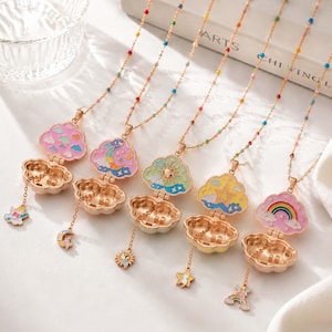 May include: Five gold-tone metal locket necklaces with cloud-shaped pendants. Each locket opens to reveal colorful enamel designs including clouds, a moon, a sun, a star, and a rainbow. The chains feature small, multi-colored beads throughout.