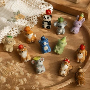 Può includere: Una collezione di dodici piccoli ciondoli in ceramica a forma di animale, ognuno con un minuscolo alimento sulla testa. Le figure includono un panda, un koala, un coniglio, una volpe, un cane, un orso, una rana, un gatto, un topo e uno scoiattolo.