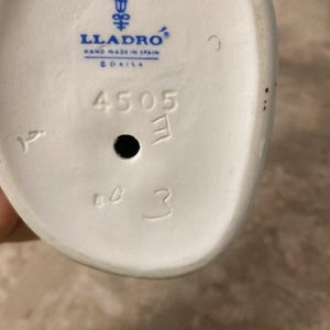 K&ouml;nnte beinhalten: Wei&szlig;er Keramikfigurensockel mit dem Lladro-Logo, "Hand Made in Spain" und dem Wort "DAISA". Der Sockel hat die Zahlen "4505", "E" und "3" aufgedruckt.