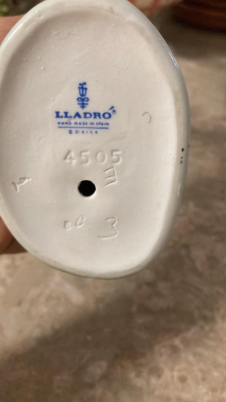 K&ouml;nnte beinhalten: Wei&szlig;er Keramikfigurensockel mit dem Lladro-Logo, "Hand Made in Spain" und dem Wort "DAISA". Der Sockel hat die Zahlen "4505", "E" und "3" aufgedruckt.