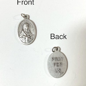 May include: Two silver-colored oval pendants. One pendant features an engraved image of a woman with the text "KATERI TEKAKWITHA". The other pendant has the text "PRAY FOR US" and "ITALY".