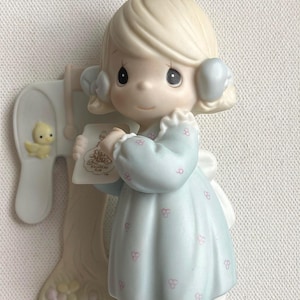 Puede incluir: Figura de porcelana de una niña con un vestido azul claro sosteniendo una carta. La figura tiene cabello rubio y está junto a un buzón con un pollito amarillo. El vestido tiene detalles florales rosas.