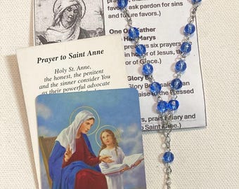 May include: A blue beaded rosary with a silver chain and a Saint Anne medal. Includes prayer cards with text about Saint Anne and the Chaplet Prayers. The cards feature illustrations of Saint Anne and the Virgin Mary.