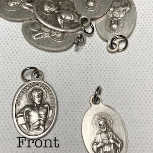 Może przedstawiać: Kolekcja srebrzystych owalnych wisiorków, każdy z małą pętlą do mocowania. Jeden wisiorek przedstawia postać z napisem "St Dismas Good Thief" i słowem "Front". Inny wisiorek przedstawia postać ze słowem "Back".