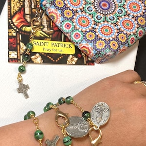 May include: A rosary bracelet with green beads and gold-coloured chain, featuring Saint Patrick medallions and a cross charm. A colourful patterned pouch and a Saint Patrick card are also visible.