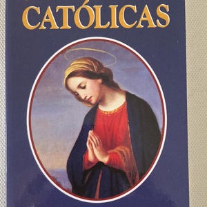Könnte beinhalten: Ein Buch mit dem Titel "ORACIONES CATÓLICAS" in goldener Schrift auf dunkelblauem Hintergrund. Das Cover zeigt ein rundes Bild einer Frau in rotem Kleid und dunkelblauem Schal, die Hände zum Gebet gefaltet. Der Text "Recopilado de fuentes tradicionales" steht darunter.