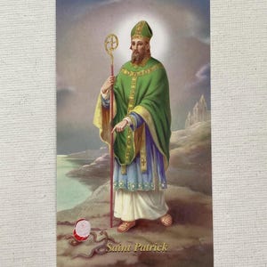 May include: A vintage postcard featuring Saint Patrick, dressed in green and gold robes, holding a staff. The image includes the text "Saint Patrick" and depicts a snake and a red and white object.