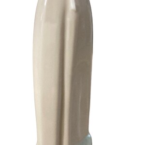 K&ouml;nnte beinhalten: Porzellanfigur einer Frau, von hinten gesehen. Die Figur tr&auml;gt ein langes, hellbeige Kleid mit einer wei&szlig;en Sch&uuml;rze, die an der Taille gebunden ist. Kopf und Schultern sind grau, der Sockel hellgr&uuml;n.