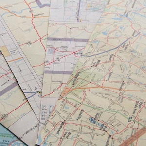 May include: A selection of old road maps, spread out to show their detailed routes and place names. The maps feature a mix of colours, with red lines highlighting roads and highways, and various text labels.