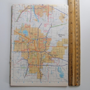 May include: A detailed map of Oklahoma City, showing roads, highways, and city names. The map is open and lying flat, next to a wooden ruler. The map is printed on paper with a grid pattern and various colours.