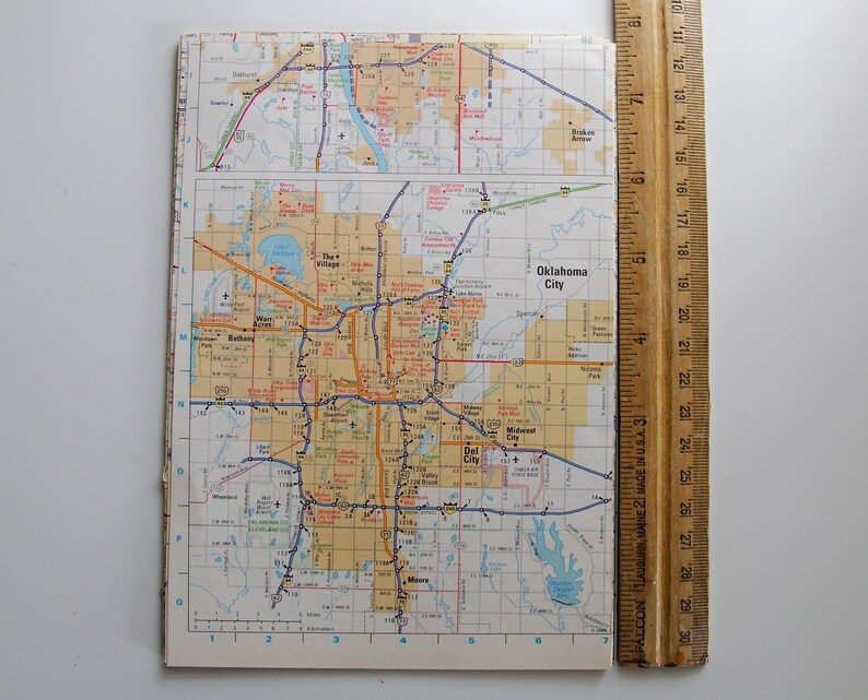 May include: A detailed map of Oklahoma City, showing roads, highways, and city names. The map is open and lying flat, next to a wooden ruler. The map is printed on paper with a grid pattern and various colours.