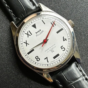 May include: A classic wristwatch featuring a white dial with black numerals and a red second hand. The watch has a silver case and a black leather strap. The face displays "hmt Pilot" and "PARA SHOCK 17 JEWELS".