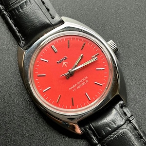 May include: A vintage wristwatch with a vibrant red face and silver-tone case. The watch features a black leather band and the text "PARA SHOCK 17 JEWELS". The watch has a classic design.