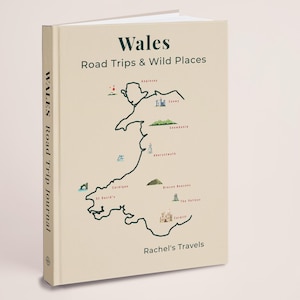 May include: A cream-colored travel journal titled "Wales Road Trips & Wild Places." The cover features a map of Wales with illustrated landmarks. The spine reads "WALES Road Trip Journal." The author's name, "Rachel's Travels," is at the bottom.