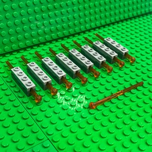 May include: Seven light gray plastic building brick components, each featuring a long, thin, translucent orange rod inserted through the center. An additional loose, long, thin, translucent orange rod is positioned separately on the green surface.