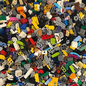 May include: A close-up shot of a pile of colorful plastic building blocks. The blocks are in various shapes and sizes, including rectangular, square, and angled pieces. Colors include red, yellow, blue, green, and gray.