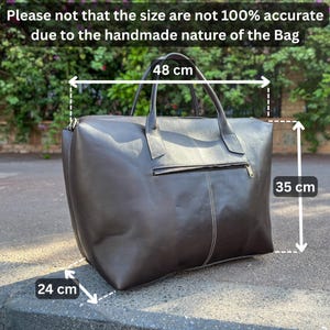 May include: A dark brown leather tote bag with a zip and two handles. The bag is 48 cm wide, 35 cm high, and 24 cm deep. The text on the image says the size is not 100% accurate due to the handmade nature of the bag.