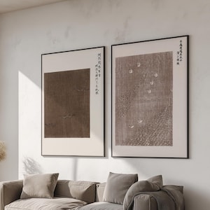 Puede incluir: Un salón moderno con una paleta de colores neutros. Dos impresiones artísticas enmarcadas con caligrafía japonesa cuelgan sobre un gran sofá seccional gris claro. Una mesa de centro de madera y una alfombra beige completan el espacio. Una gran ventana ofrece vistas al exterior.