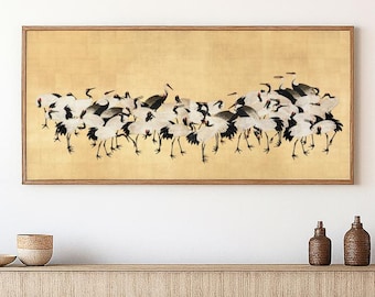 May include: A framed artwork featuring a flock of cranes in black and white against a gold background. The artwork is displayed above a wooden console table with decorative items.
