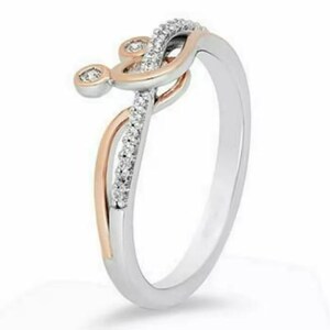 Pode incluir: Um anel de prata com um design &uacute;nico. O anel apresenta um detalhe em ouro rosa e um topo decorativo adornado com pequenas pedras brilhantes. O design inclui um redemoinho e uma pequena pedra redonda.