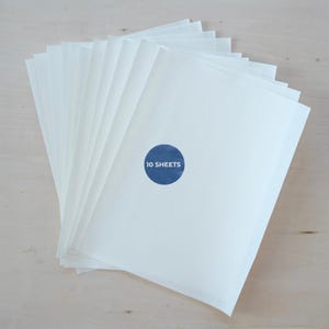 May include: A stack of white paper sheets with a blue circular sticker that reads "10 SHEETS". The paper is arranged in a fan shape, with the sticker placed on the front sheet.
