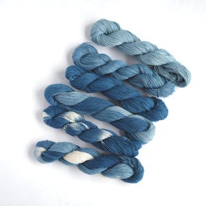 May include: A collection of blue yarn skeins, each a different shade of blue, arranged in a gradient from light to dark.