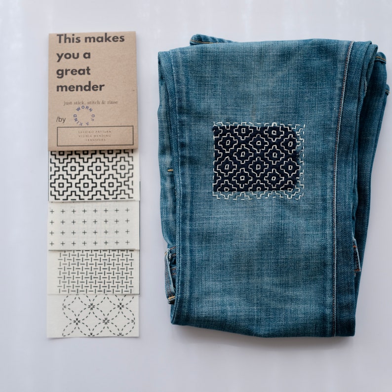 Puede incluir: Un conjunto de cinco patrones de reparaci&oacute;n sashiko en tela blanca con costuras negras. El texto en la tarjeta marr&oacute;n dice "This makes you a great mender. Just stick, stitch & rinse. by Worn & Kind. Sashiko Pattern Vintage & Modern Transfers". Un par de pantalones vaqueros azules con un parche sashiko en la rodilla.