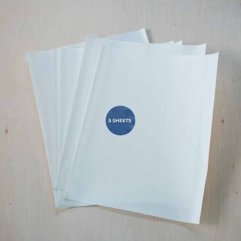 May include: A stack of five white paper sheets. A blue circular sticker on the top sheet reads "5 SHEETS". The paper has a slightly translucent quality, and the background is a light wood grain.