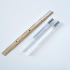 May include: Two clear plastic pens and a wooden ruler with black markings. The ruler is about 12 inches long.