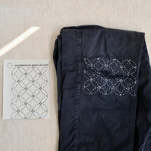 Puede incluir: Un par de pantalones vaqueros azul oscuro con un dise&ntilde;o bordado blanco en la rodilla. El dise&ntilde;o es un patr&oacute;n repetitivo de c&iacute;rculos y estrellas. Los vaqueros est&aacute;n doblados por la mitad y sobre una superficie beige claro. El texto "wornofakind.com @worn_of_a_kind" est&aacute; impreso en una tarjeta blanca junto a los vaqueros.