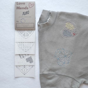 Peut inclure: Un ensemble de quatre motifs de broderie thermocollants en forme de cœurs. Les motifs sont sur du papier blanc et présentent différents motifs de points. Les motifs sont étiquetés "Love Mends XOXO" et "Worn & Kind Pre-Printed Visible Mending Transfers".