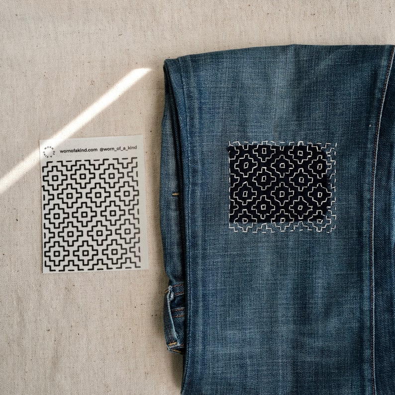 Puede incluir: Un par de pantalones vaqueros azules con un patr&oacute;n geom&eacute;trico blanco y negro cosido en el bolsillo trasero. El patr&oacute;n est&aacute; delineado con hilo blanco. El texto "wornofakind.com @worn_of_a_kind" est&aacute; impreso en una tarjeta blanca junto a los vaqueros.