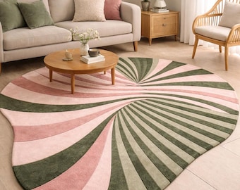 Puede incluir: Una alfombra ovalada con un diseño en espiral en tonos rosa y verde oliva. La alfombra está colocada en un salón, con un sofá, una mesa de centro y una silla en el fondo. El diseño de la alfombra crea un punto focal.
