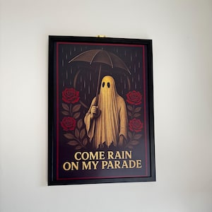 Könnte beinhalten: Gerahmter Kunstdruck mit einer Geisterfigur unter einem Regenschirm im Regen, umgeben von roten Rosen. Der Text "COME RAIN ON MY PARADE" ist in goldener Schrift dargestellt. Das Kunstwerk ist vor einem dunklen Hintergrund.