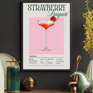 May include: Framed art print featuring a Strawberry Daiquiri cocktail. The image shows a pink background with a cocktail glass filled with a red drink, garnished with a strawberry. The ingredients are listed below the image.