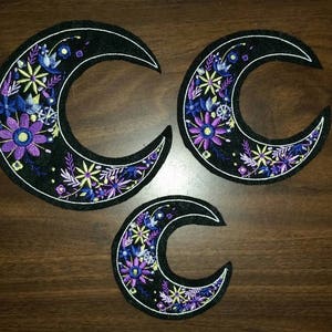 May include: Three black felt crescent moon patches with embroidered purple, blue, and yellow flowers.