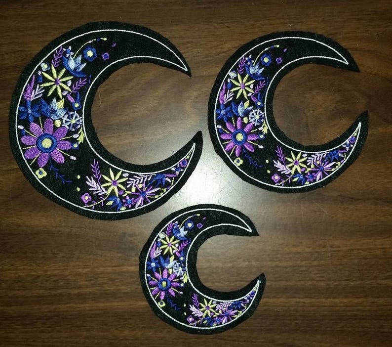 May include: Three black felt crescent moon patches with embroidered purple, blue, and yellow flowers.