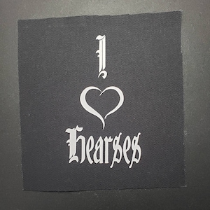 May include: A black fabric patch with white lettering that reads "I ♥ Hearses". The heart is stylized and the lettering is in a gothic font.