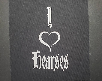 Op de afbeelding: Een zwarte stoffen patch met witte tekst die "I ♥ Hearses" zegt. Het hart is gestileerd en de tekst is in een gotisch lettertype.