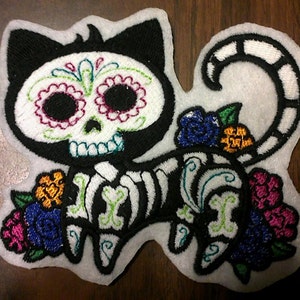 May include: Embroidered iron-on patch of a black and white cat with a sugar skull face, skeleton body, and colorful flowers.