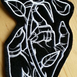 May include: Black embroidered patch with a white outline of a rose with leaves and stem.