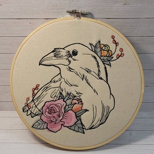May include: Embroidered hoop art featuring a black and white raven with a pink and orange rose and foliage.