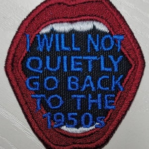 May include: A red embroidered patch shaped like a mouth with a white set of teeth. The mouth is open and the text "I WILL NOT QUIETLY GO BACK TO THE 1950S" is written in blue on a black background.